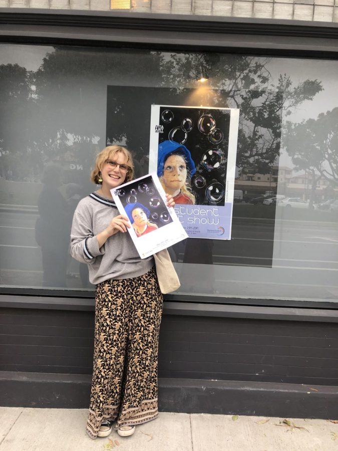 Senior Kenzie Herbert is standing in front of her art piece Love and Bubbles which was chosen to be on display in the front window of the Vita Art Center.