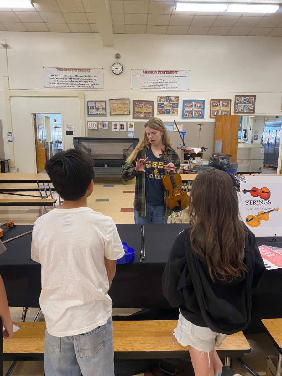 Two kids watch as freshman Avery Verardo shows them how to play a violin 