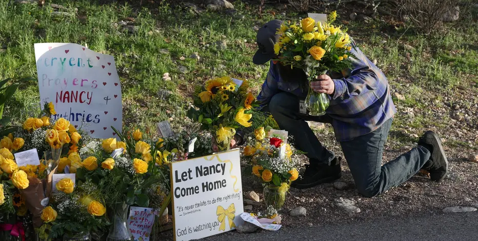 A man kneeling at a crowd of flowers for missing Nancy Guthrie.