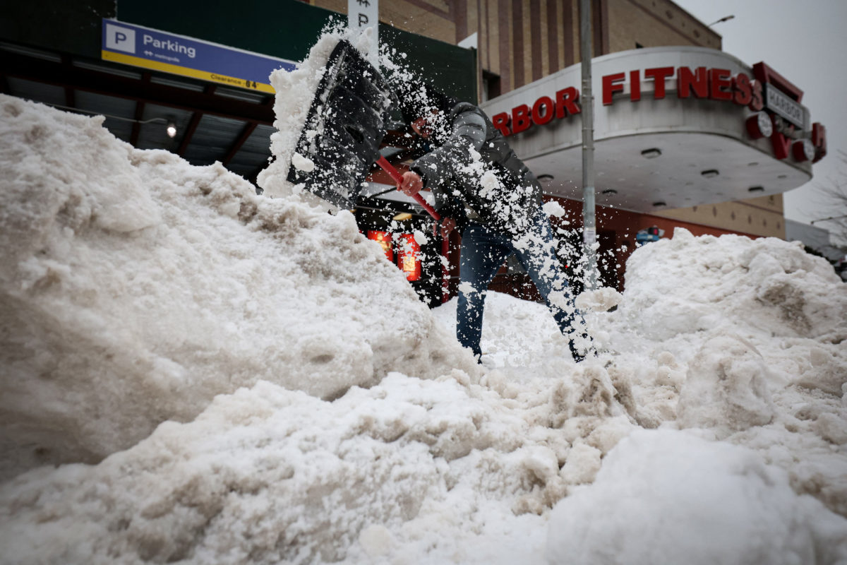 A worker shoveling snow from the entrance of a parking lot.
