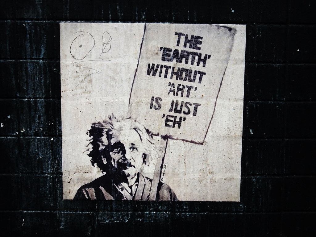 Albert Einstein holding up a poster that says, "The 'Earth' Without 'Art' Is 'Eh'".