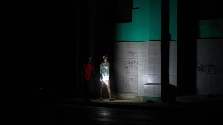 On Saturday March 21, 2026, people walk down a dark street in Havana, using  flashlights to see.